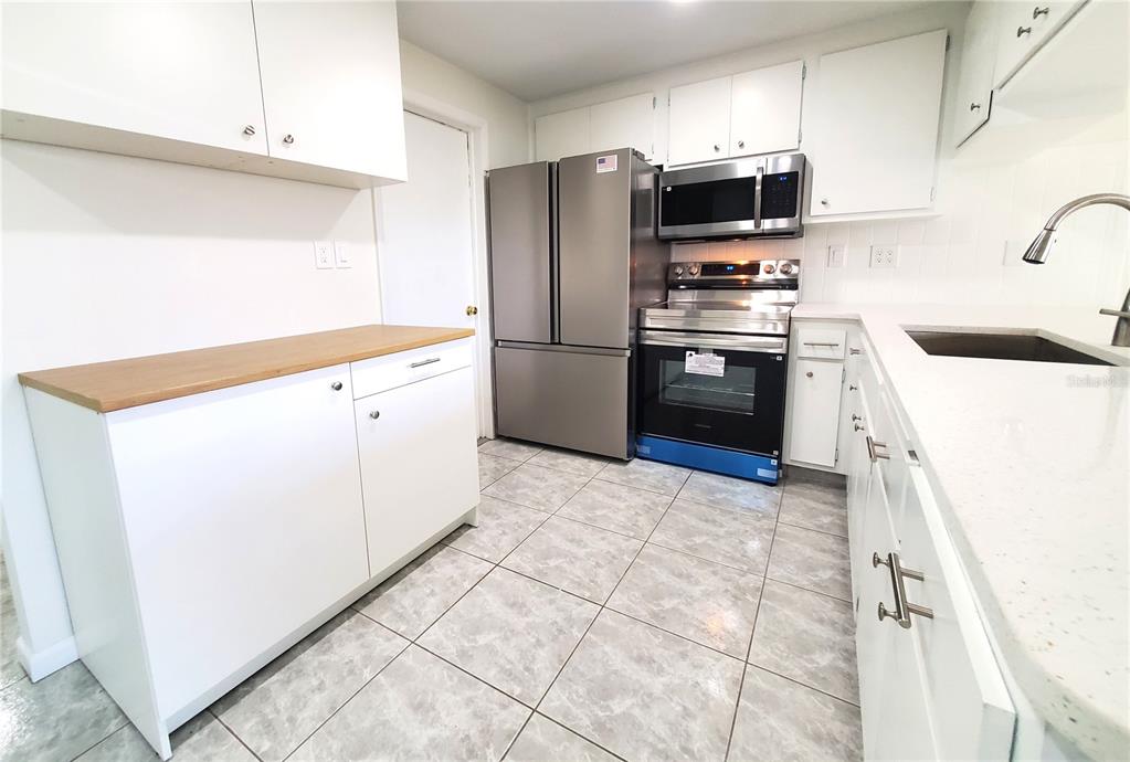 A kitchen features white cabinets, stainless steel appliances, a wood countertop, and gray tiled flooring — 7534 ROSEWOOD DRIVE, PORT RICHEY, FL