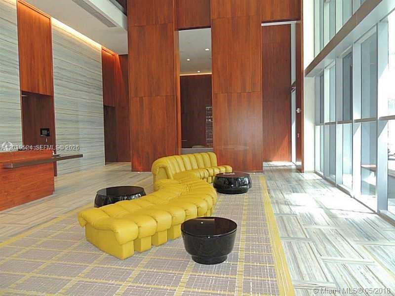 A modern lobby features a yellow curved sofa, black coffee tables, and wood-paneled walls — 1300 Brickell Bay Dr # 1707, Miami FL 33131, MIAMI, FL