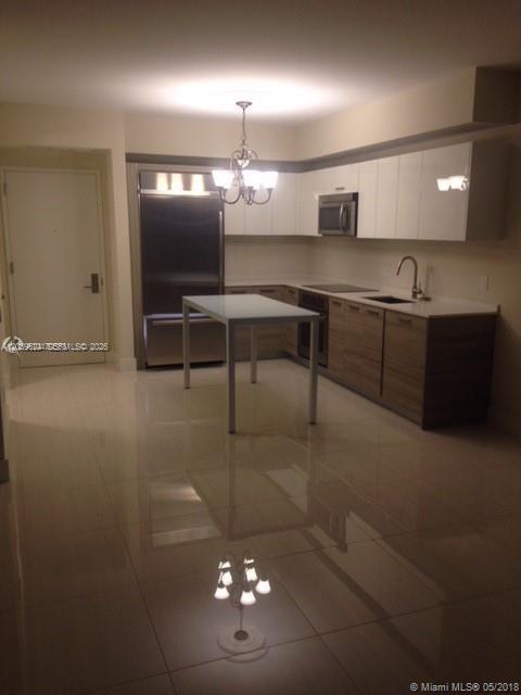 A modern kitchen features white upper cabinets, wood-toned lower cabinets, and a central dining table — 1300 Brickell Bay Dr # 1707, Miami FL 33131, MIAMI, FL