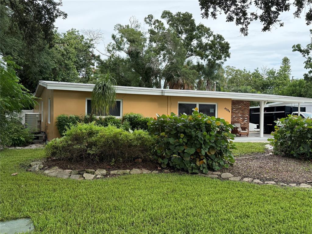 A single-story yellow house features a front yard with landscaping and a covered carport — 4394 POMPANO DRIVE SE, ST PETERSBURG, FL