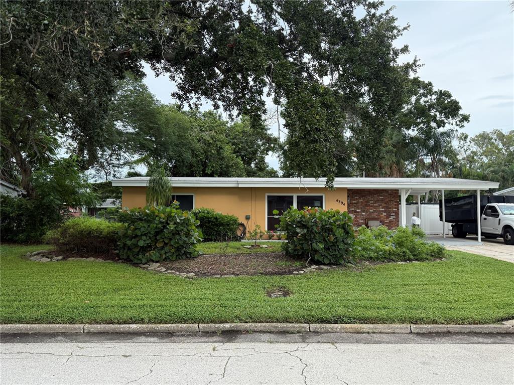 A single-story house with a yellow exterior, brick accents, and a carport sits behind landscaping — 4394 POMPANO DRIVE SE, ST PETERSBURG, FL