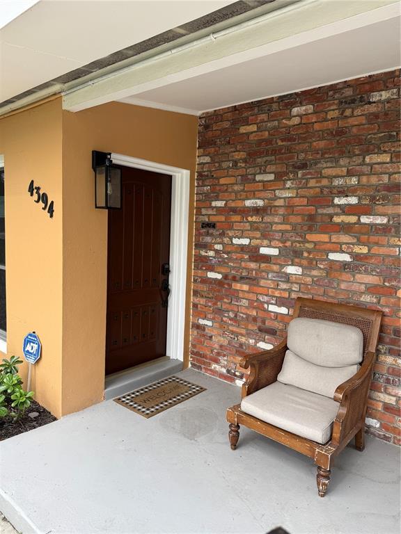 A front porch features a brown door, a brick wall, and a wooden armchair — 4394 POMPANO DRIVE SE, ST PETERSBURG, FL