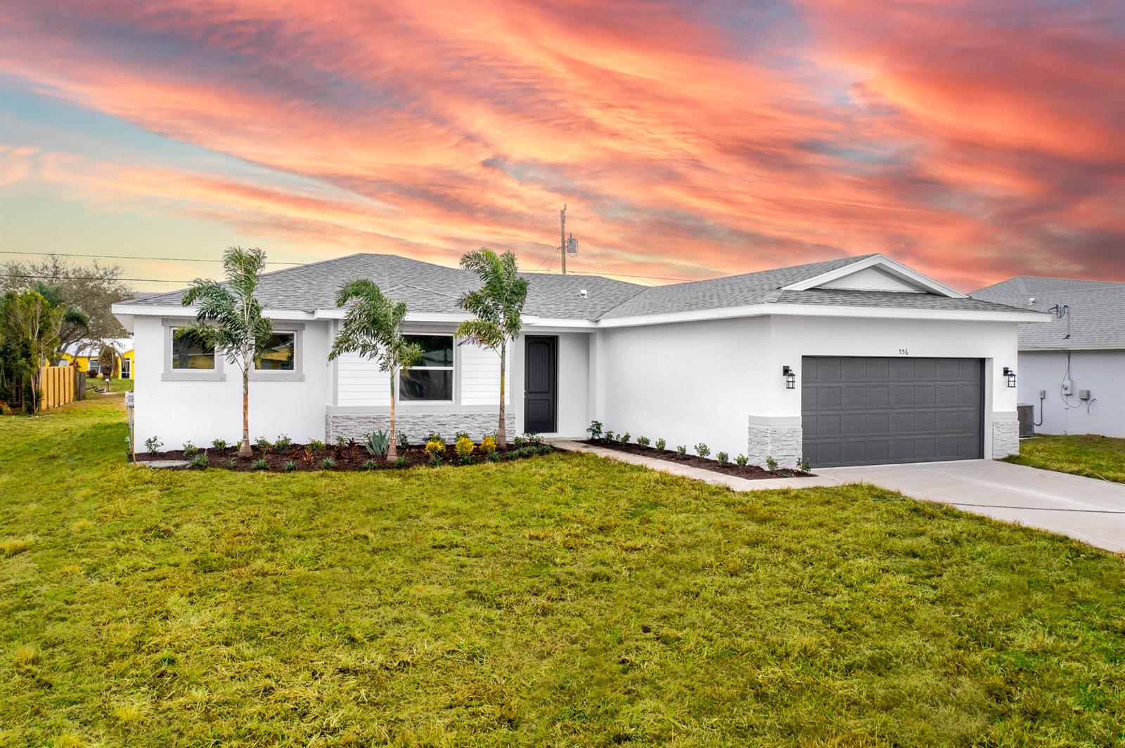 A white single-story house with a gray garage door and palm trees at sunset — 5303 Sunset Boulevard, Fort Pierce FL 34982, FORT PIERCE, FL
