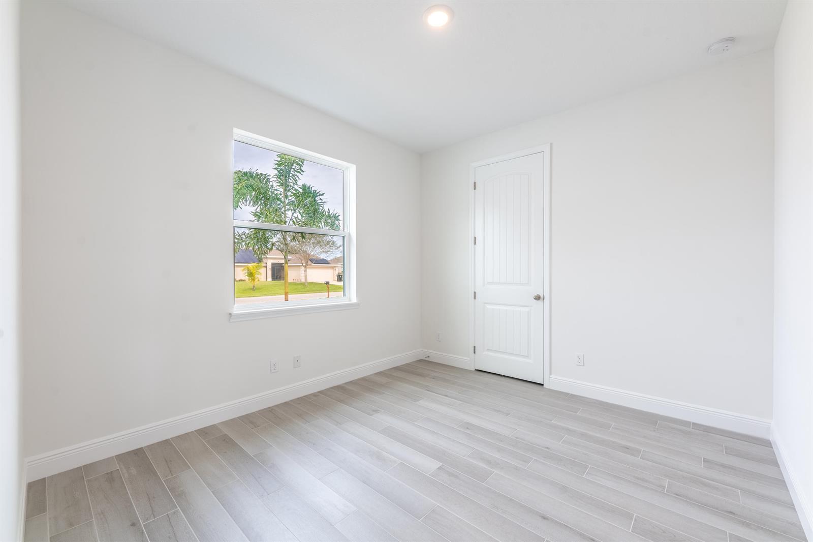 An empty bedroom features white walls, light gray wood-look tile flooring, and a single window — 5303 Sunset Boulevard, Fort Pierce FL 34982, FORT PIERCE, FL