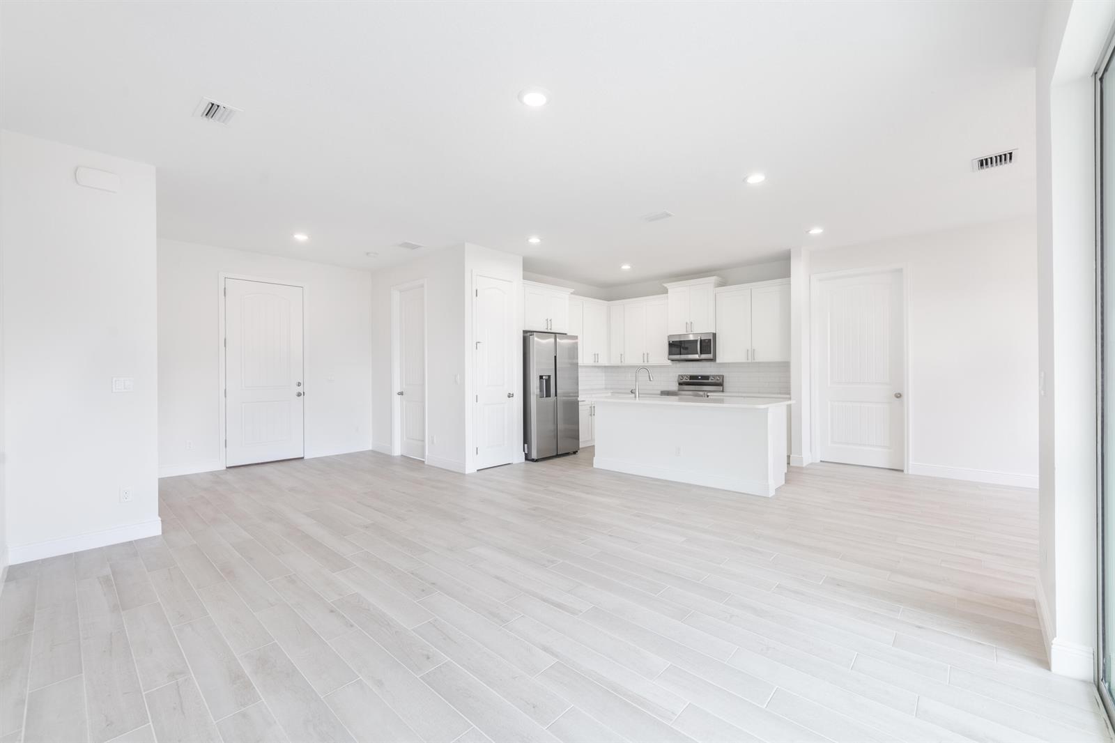 An open-concept kitchen and living area features white cabinetry, stainless steel appliances, and light flooring — 5303 Sunset Boulevard, Fort Pierce FL 34982, FORT PIERCE, FL