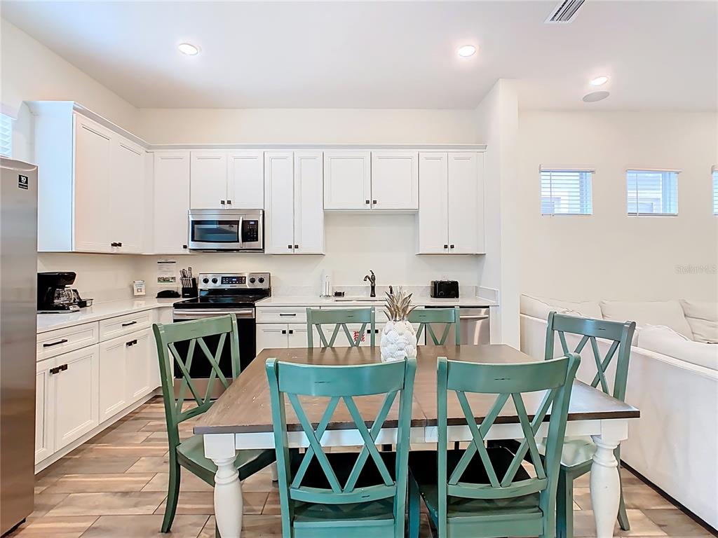 A kitchen with white cabinetry and stainless steel appliances sits behind a wooden dining table — 2946 SALTED RIM ROAD, KISSIMMEE, FL