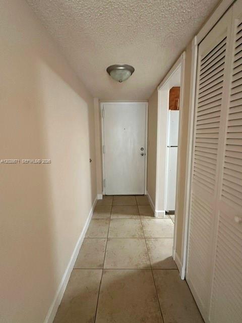 A hallway with beige tile flooring leads to a white door and a kitchen area — 14250 SW 62nd St # 221, Miami FL 33183, MIAMI, FL