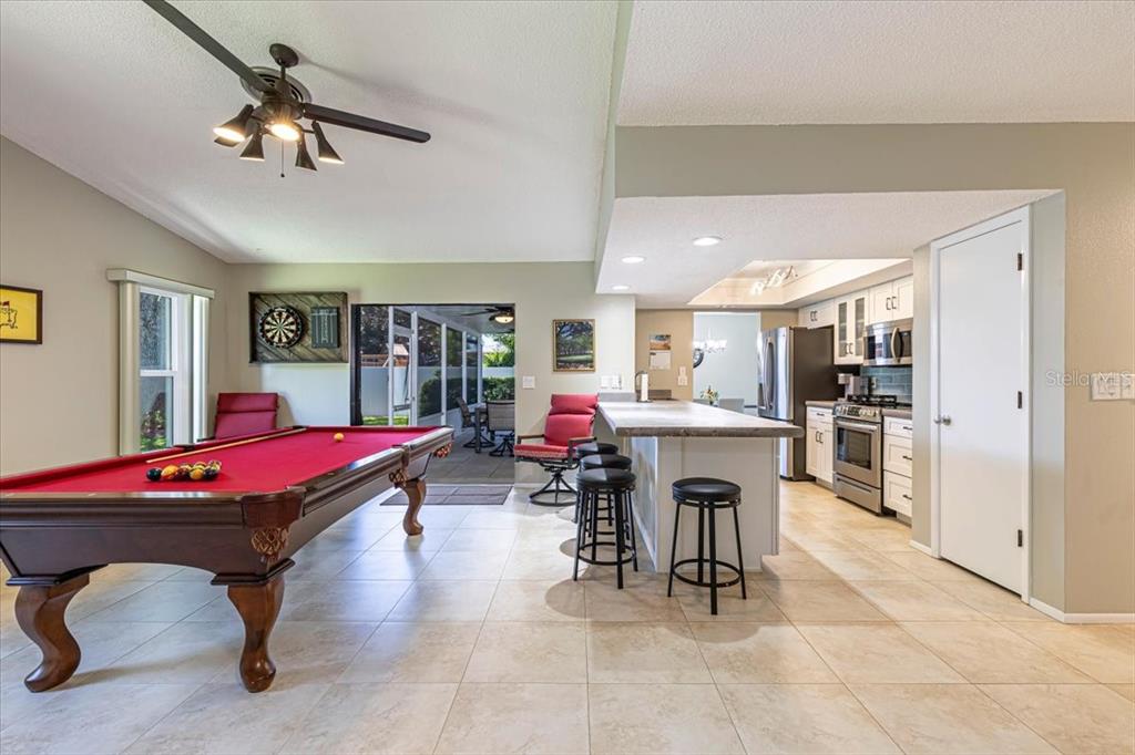 A room featuring a red pool table, a kitchen island with bar stools, and tile flooring — 1234 PINEBROOK WAY, VENICE, FL