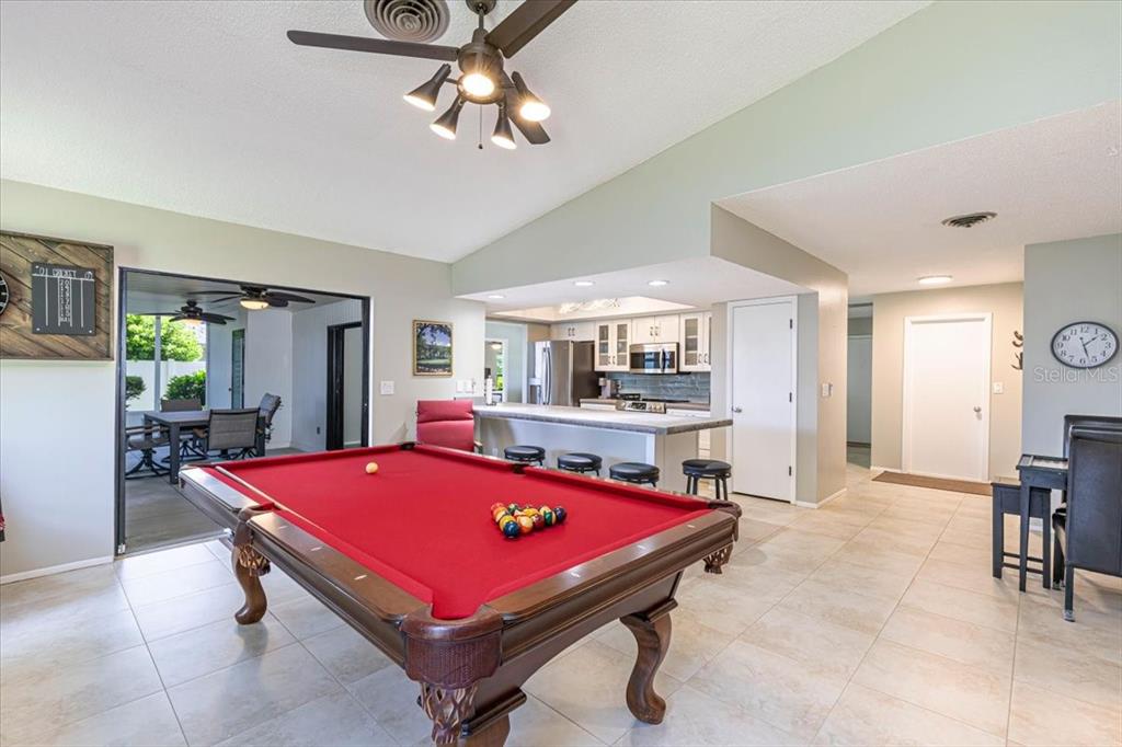 A game room with a red pool table, tile flooring, and an open-concept kitchen — 1234 PINEBROOK WAY, VENICE, FL