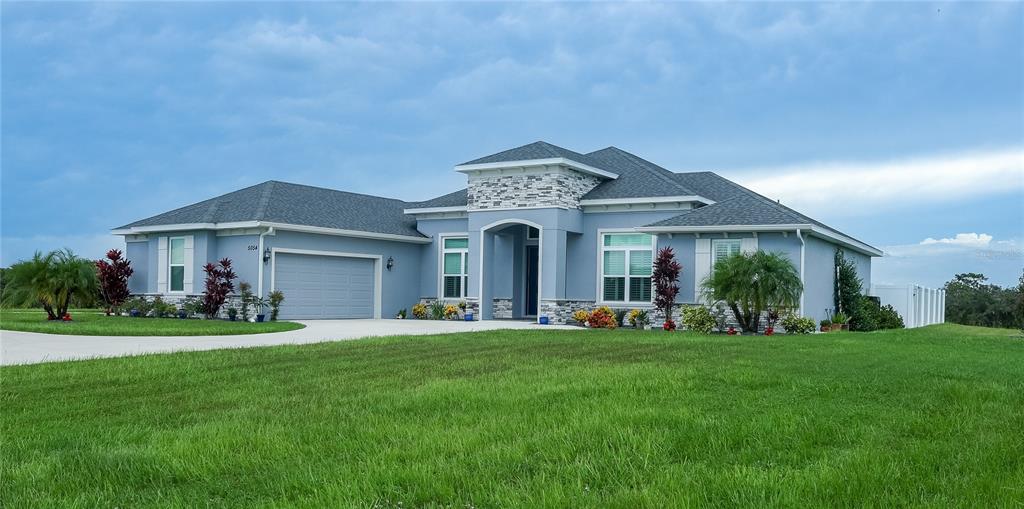 A single-story blue house with a stone-accented entryway and a two-car garage — 5054 LAKE TOSCANA DRIVE, WIMAUMA, FL