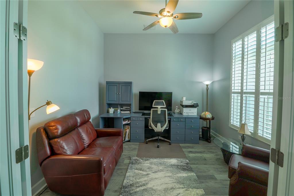 A home office features a leather sofa, a blue desk with a computer, and plantation shutters — 5054 LAKE TOSCANA DRIVE, WIMAUMA, FL