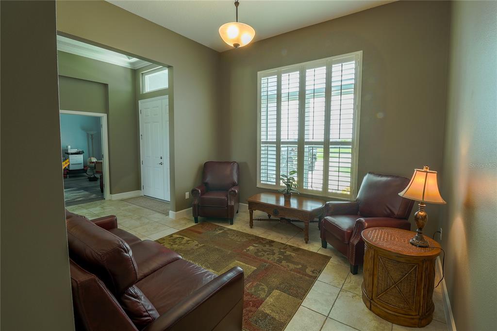 A living room features tile flooring, leather furniture, a wooden coffee table, and plantation shutters — 5054 LAKE TOSCANA DRIVE, WIMAUMA, FL