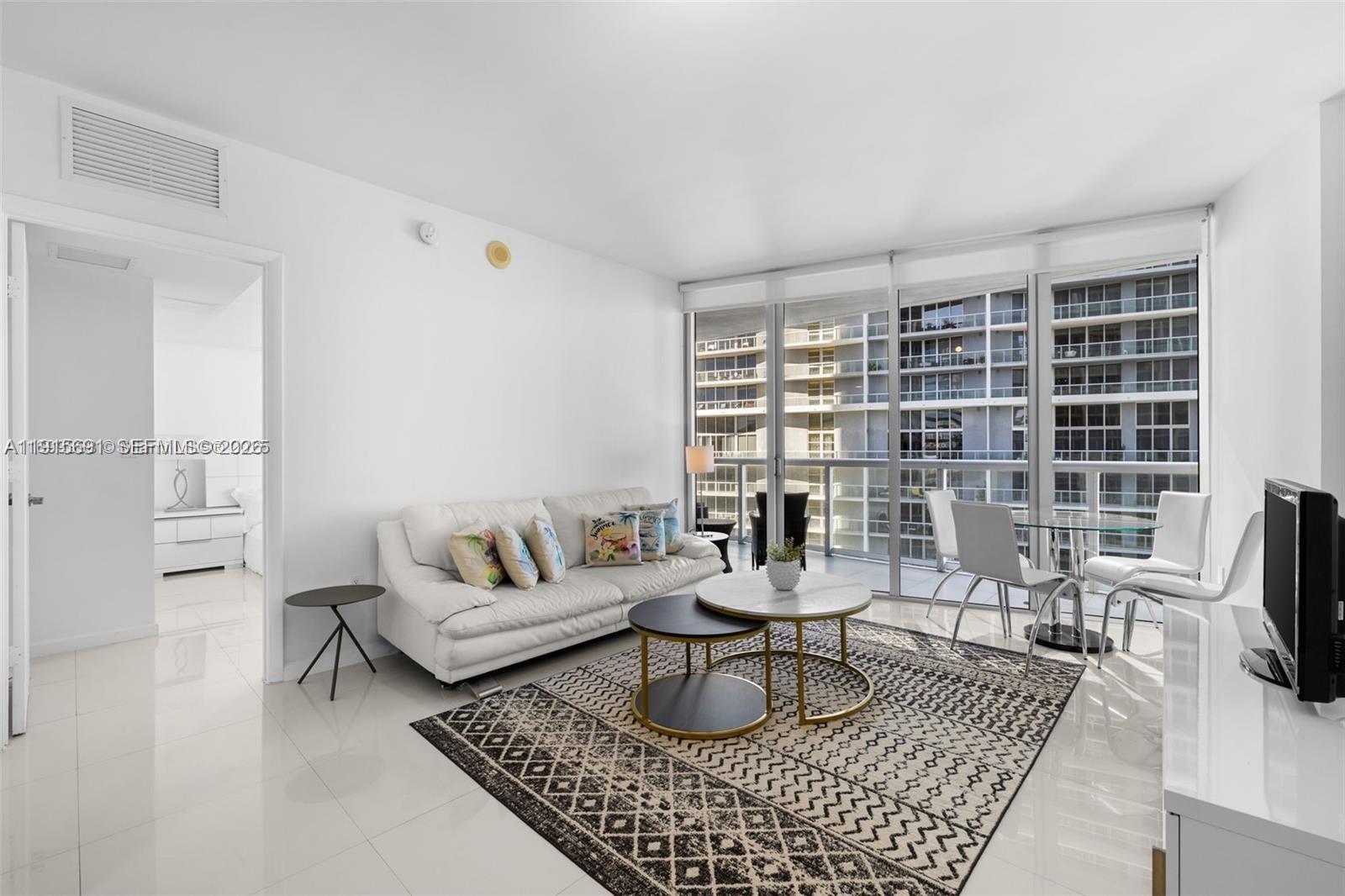 A bright living room features white tile floors, a white sofa, and floor-to-ceiling windows — 495 Brickell Ave # 2206, Miami FL 33131, MIAMI, FL