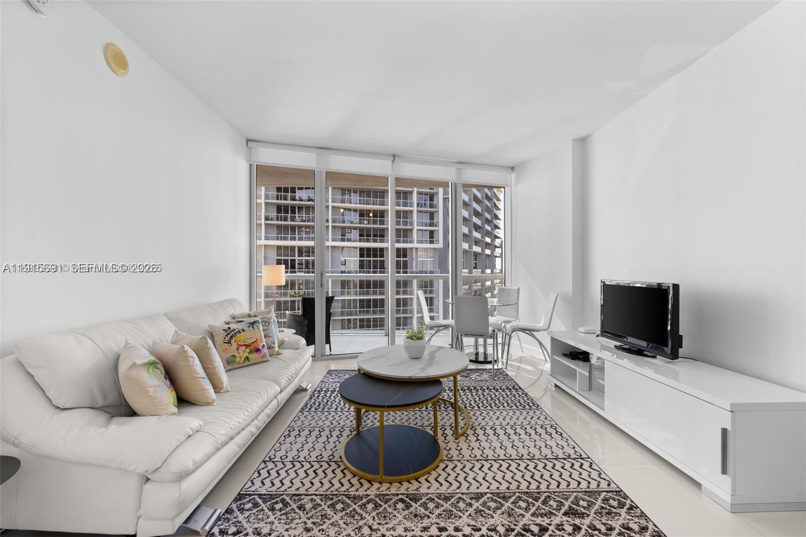 A living room features a white sofa, a patterned rug, and a glass balcony door — 495 Brickell Ave # 2206, Miami FL 33131, MIAMI, FL