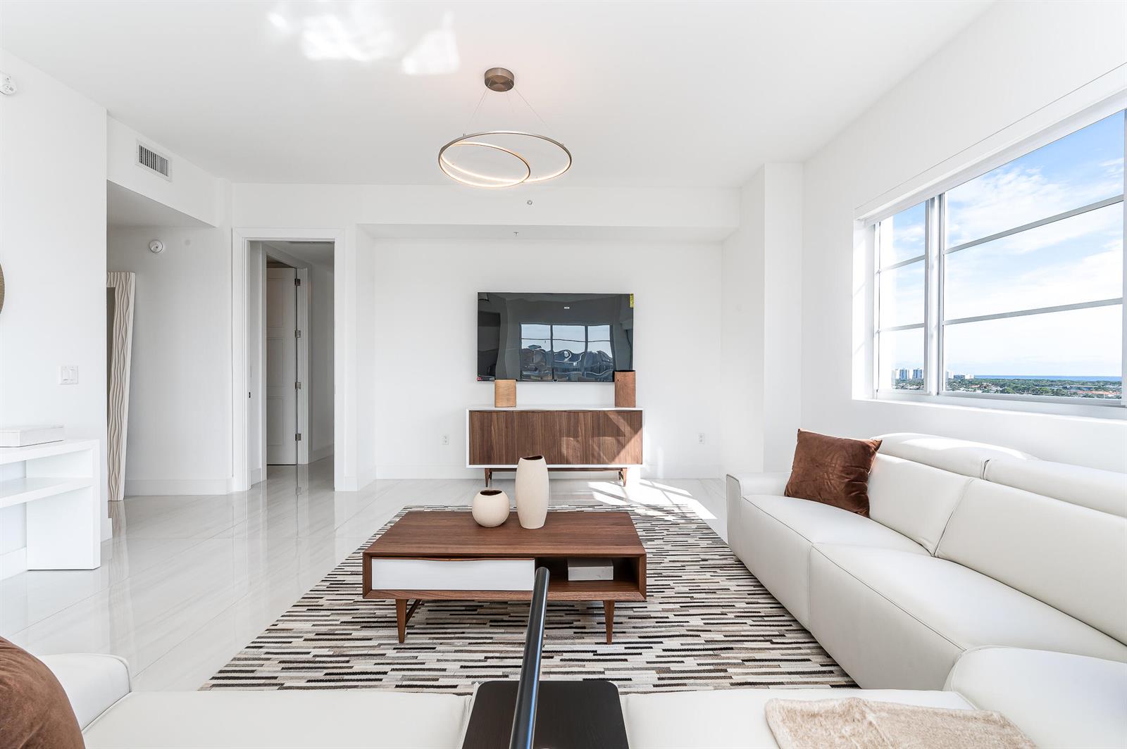 A bright living room features a white sofa, a wooden coffee table, and a wall-mounted television — 155 E Boca Raton Road # 1103, Boca Raton FL 33432, BOCA RATON, FL