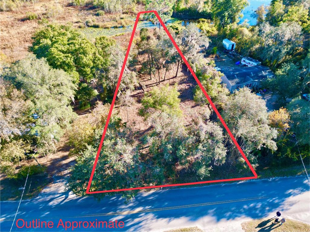 An aerial view shows a triangular, tree-covered vacant lot bordering a paved road and water — Lot 66 & Lot 67 Ashley STREET, HAWTHORNE, FL