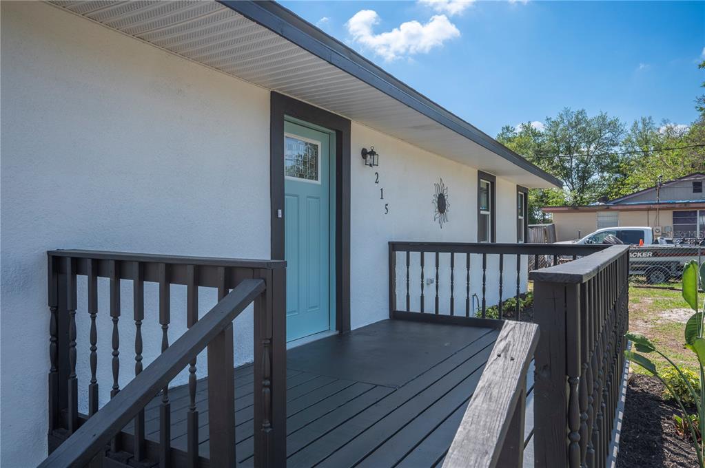 A wooden deck with dark railings leads to a light blue front door of a house — 1215 EL CAMINO ROAD, LAKELAND, FL
