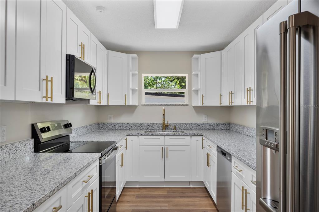 A galley kitchen features white cabinets, granite countertops, stainless steel appliances, and wood-look flooring — 1215 EL CAMINO ROAD, LAKELAND, FL