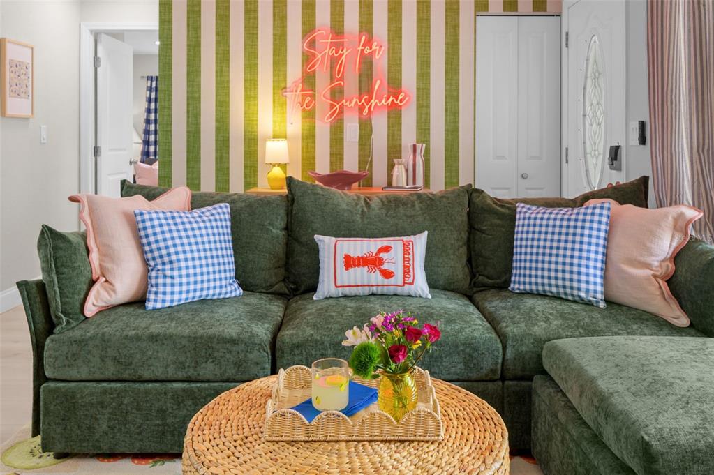 A living room features a green sectional sofa, a round wicker coffee table, and striped wallpaper — 7957 COTTONWOODE DRIVE, LARGO, FL