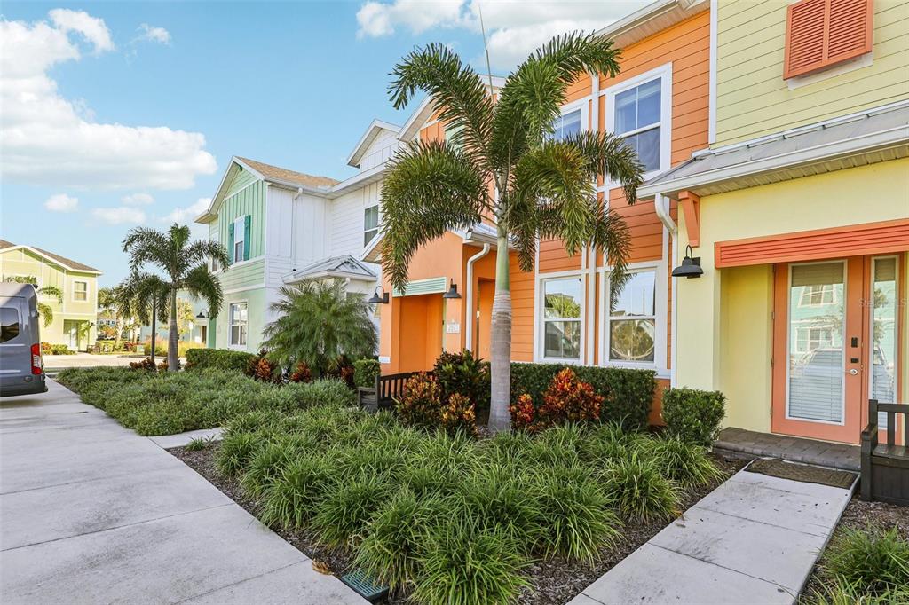 A row of colorful townhouses with palm trees and landscaped gardens under a blue sky — 2971 CASTAWAY LANE, KISSIMMEE, FL