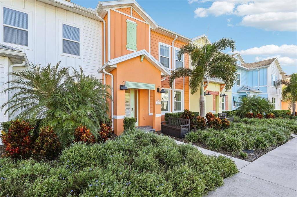 A colorful row of townhouses features palm trees, landscaping, and a sidewalk in the foreground — 2971 CASTAWAY LANE, KISSIMMEE, FL