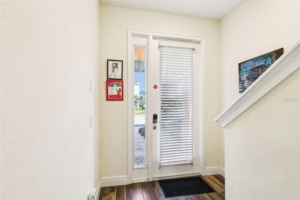 An entryway features a white front door with blinds, wood-look flooring, and a staircase railing — 2971 CASTAWAY LANE, KISSIMMEE, FL