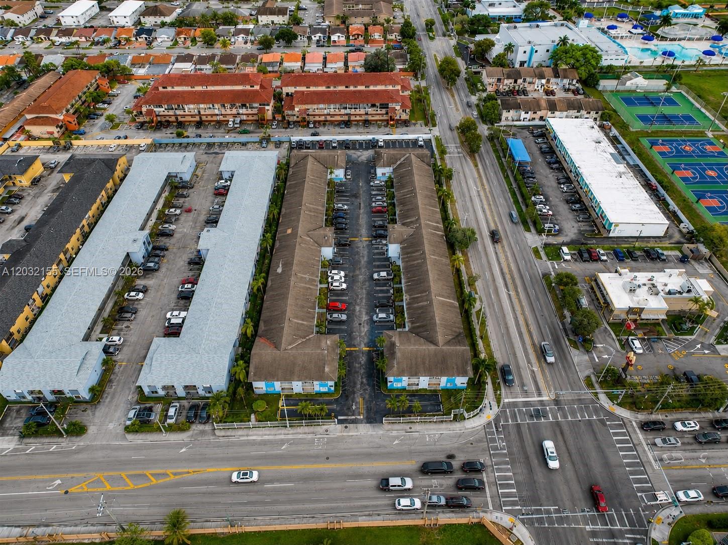 An aerial view shows residential apartment buildings with parking lots and nearby commercial properties — 6081 W 24th Ave # 102, Hialeah FL 33016, HIALEAH, FL