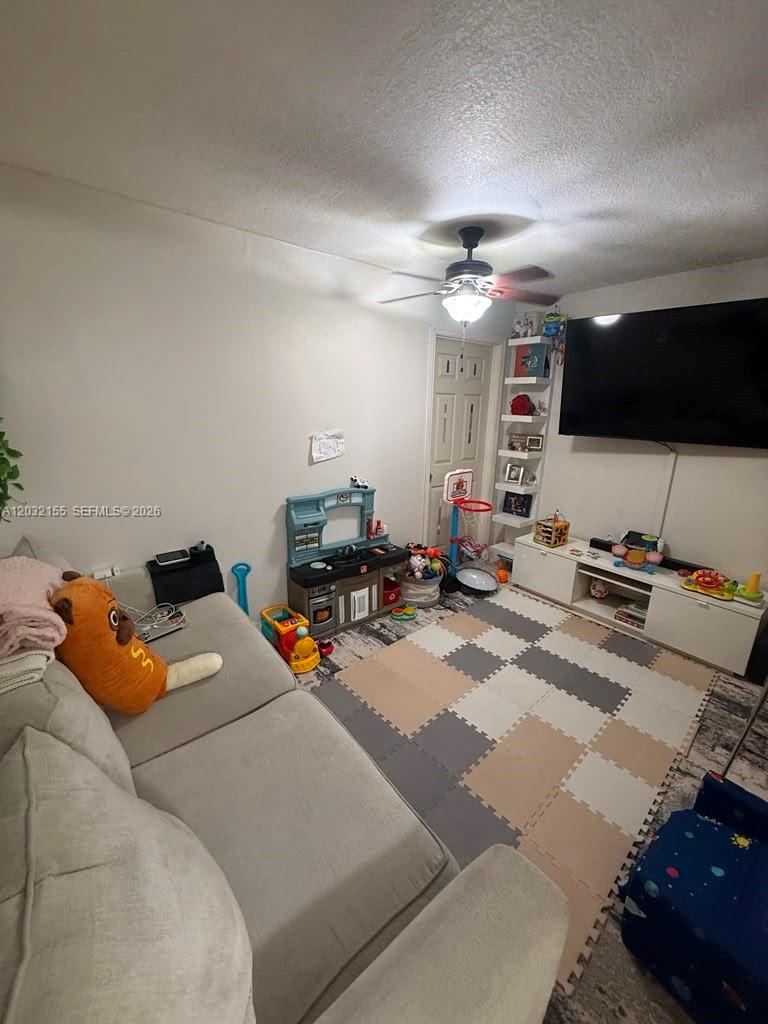 A living room with a sofa, a television, a toy kitchen, and foam floor tiles — 6081 W 24th Ave # 102, Hialeah FL 33016, HIALEAH, FL