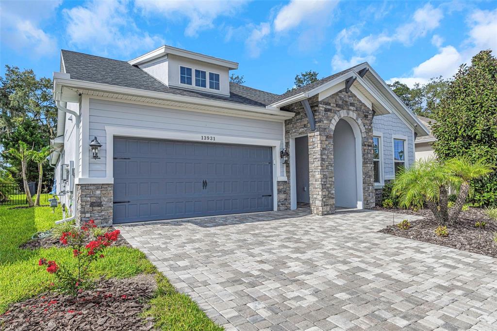 A single-story house exterior features a stone-accented arched entryway, gray garage door, and paver driveway — 13931 NATURES RESERVE DRIVE, LITHIA, FL