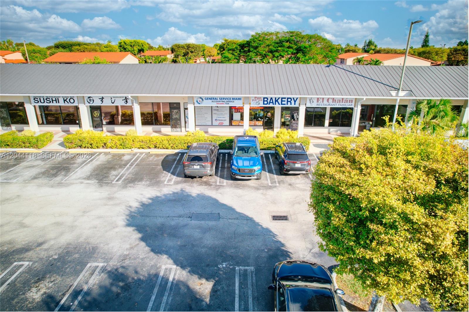 An exterior view of a commercial strip mall with a parking lot in front — MIAMI, FL