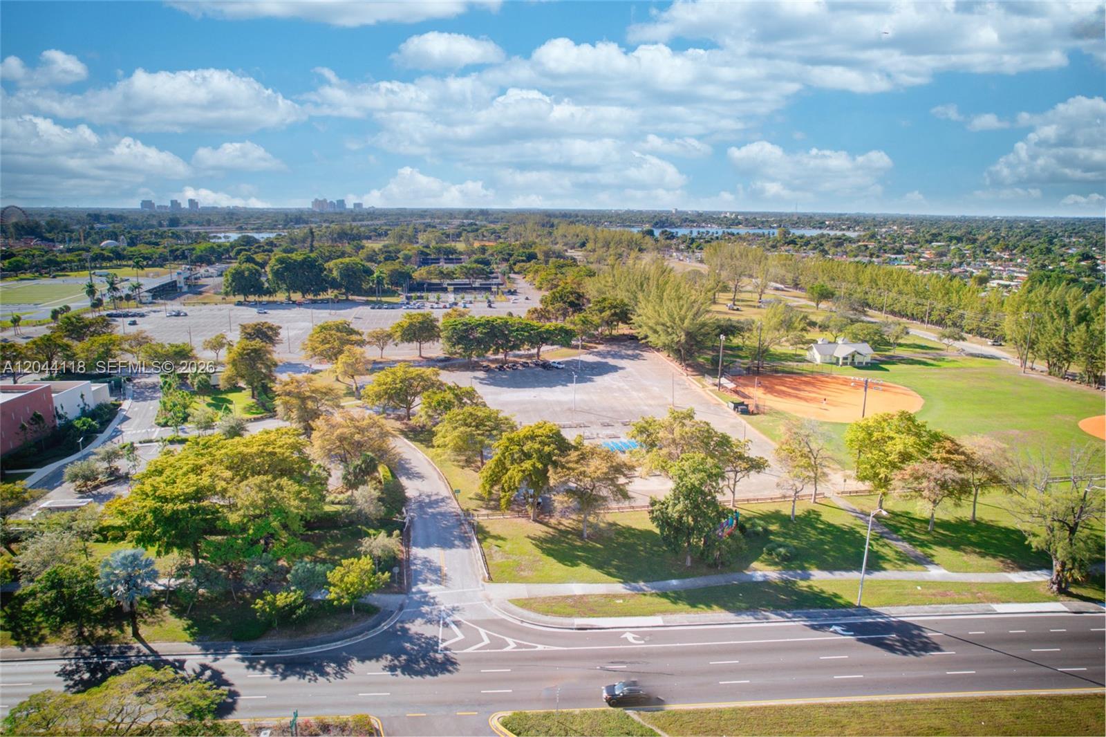 An aerial view shows a large parking lot, baseball fields, and green space near a road — MIAMI, FL