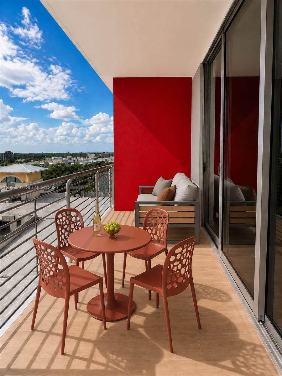 A balcony features a round table with four chairs, a sofa, and a red wall — 90 NE 32ND ST # 923, Miami FL 33137, MIAMI, FL