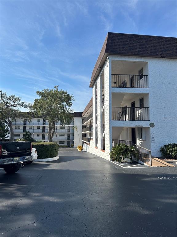 A multi-story apartment building exterior features white stucco walls, dark balconies, and a parking lot — 118 S HALIFAX AVENUE UNIT 210, DAYTONA BEACH, FL