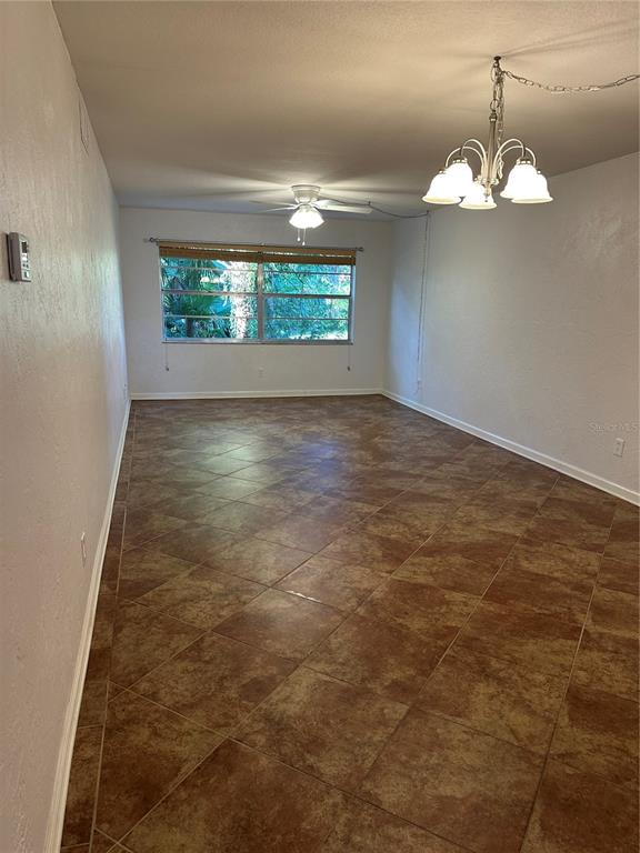 An empty room features brown tile flooring, a ceiling fan, and a hanging light fixture — 118 S HALIFAX AVENUE UNIT 210, DAYTONA BEACH, FL