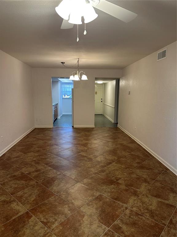 An interior view of a room with brown tile flooring, a ceiling fan, and chandelier — 118 S HALIFAX AVENUE UNIT 210, DAYTONA BEACH, FL