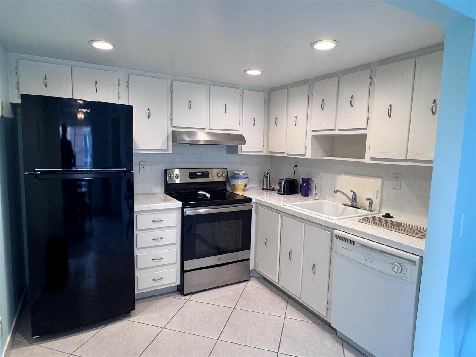 A kitchen with white cabinets, stainless steel appliances, a black refrigerator, and tiled flooring — 641 Burgundy N, Delray Beach FL 33484, DELRAY BEACH, FL