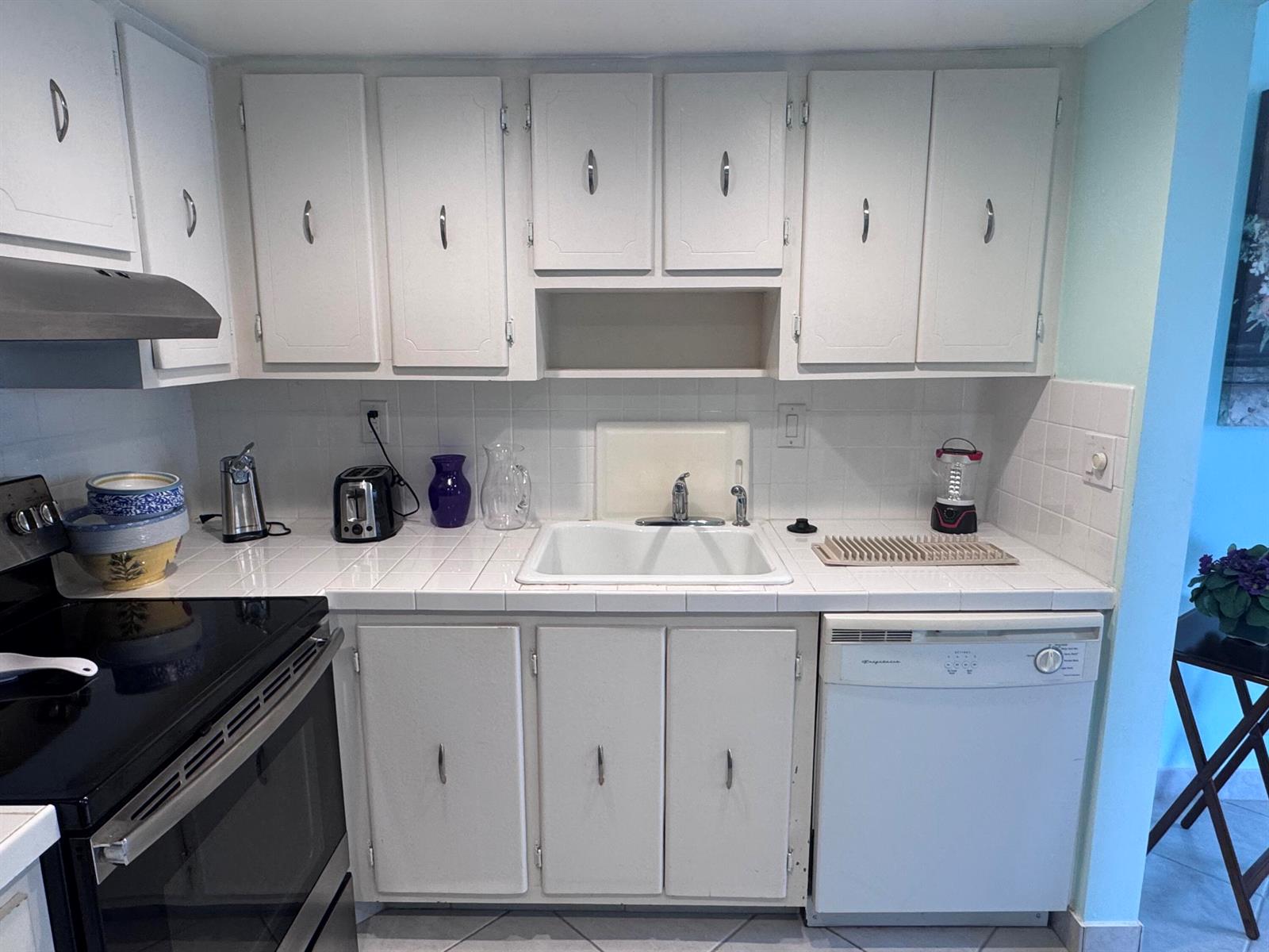 A kitchen features white cabinets, a tiled countertop, a white sink, and a dishwasher — 641 Burgundy N, Delray Beach FL 33484, DELRAY BEACH, FL