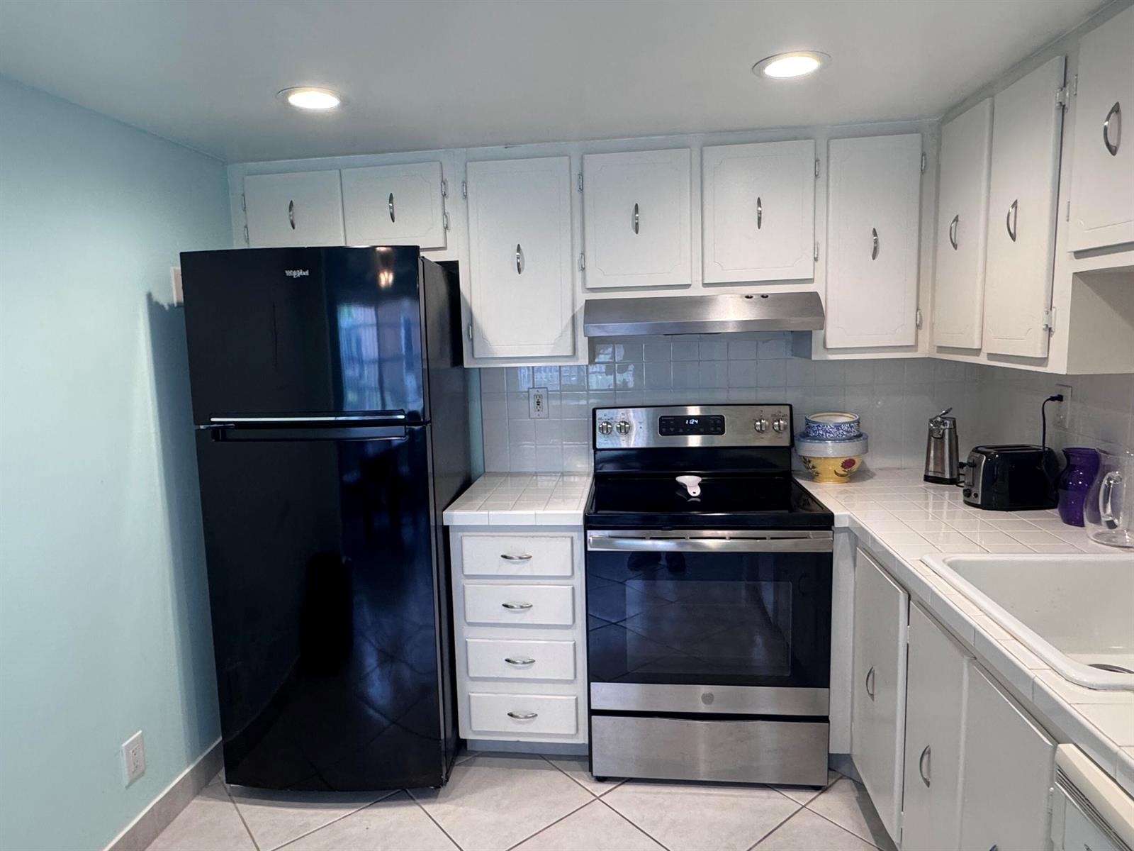 A kitchen features white cabinets, a black refrigerator, a stainless steel stove, and tiled counters — 641 Burgundy N, Delray Beach FL 33484, DELRAY BEACH, FL