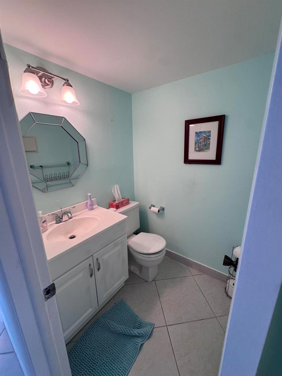 A bathroom with light blue walls, a white vanity, a mirror, and a toilet — 641 Burgundy N, Delray Beach FL 33484, DELRAY BEACH, FL