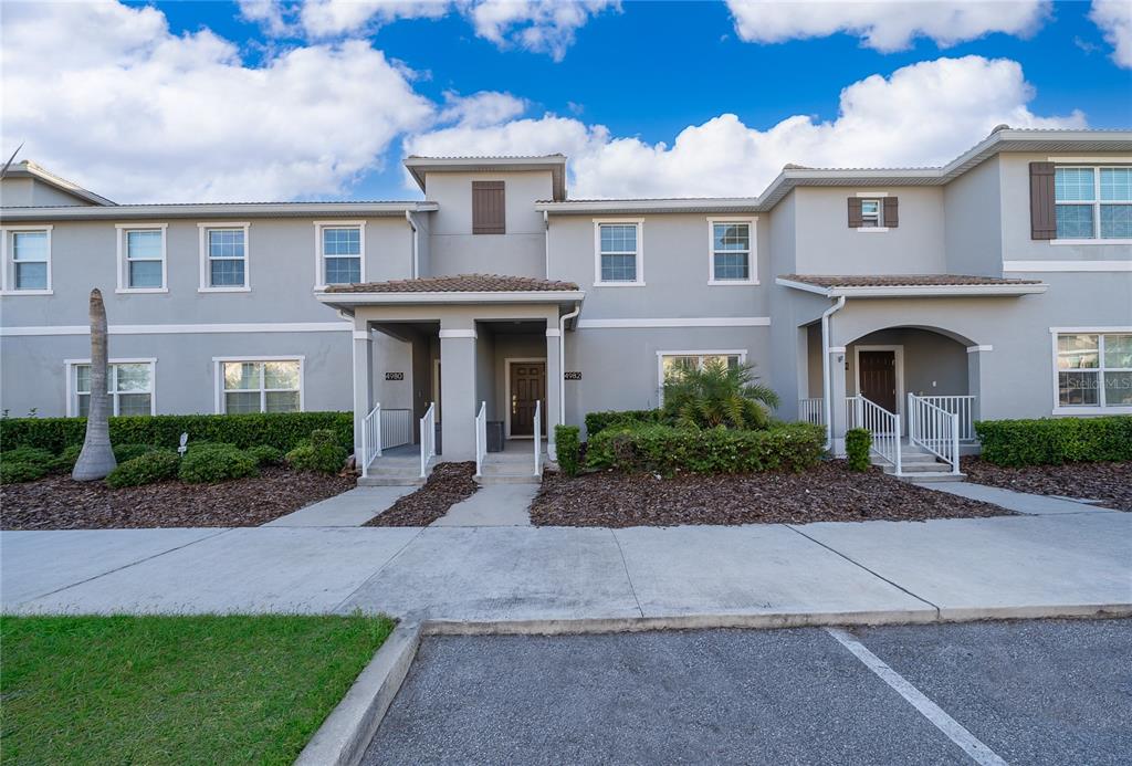 A two-story townhouse exterior with gray stucco walls, brown shutters, and a concrete walkway — 4982 WINDERMERE AVENUE, KISSIMMEE, FL