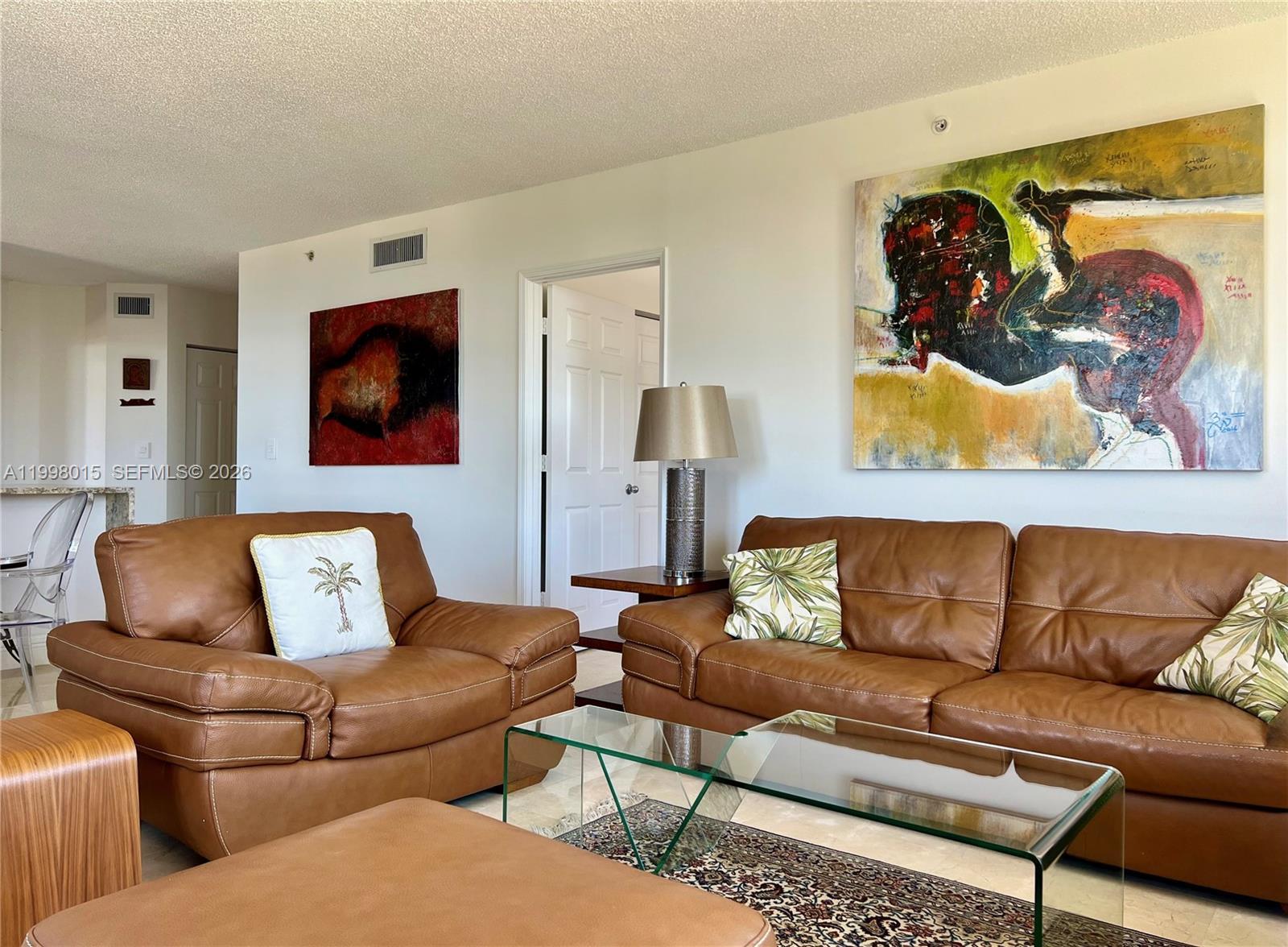 A living room features brown leather sofas, a glass coffee table, and large abstract paintings — 651 Okeechobee Blvd # 811, West Palm Beach FL 33401, WEST PALM BEACH, FL