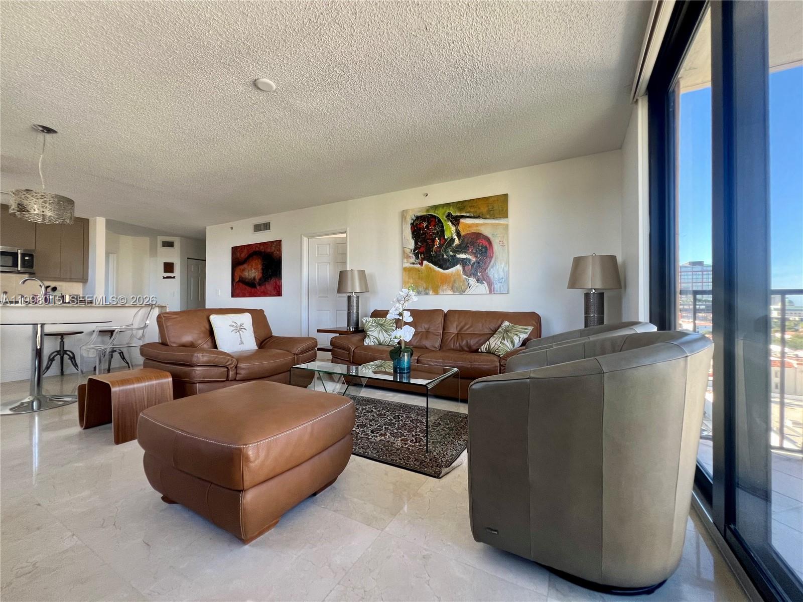 A living room features brown leather furniture, a glass coffee table, and large sliding glass doors — 651 Okeechobee Blvd # 811, West Palm Beach FL 33401, WEST PALM BEACH, FL