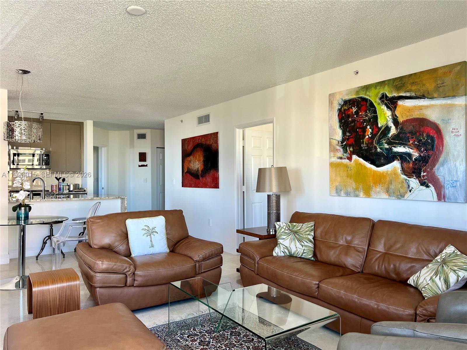 A living room features brown leather furniture, a glass coffee table, and large abstract paintings — 651 Okeechobee Blvd # 811, West Palm Beach FL 33401, WEST PALM BEACH, FL