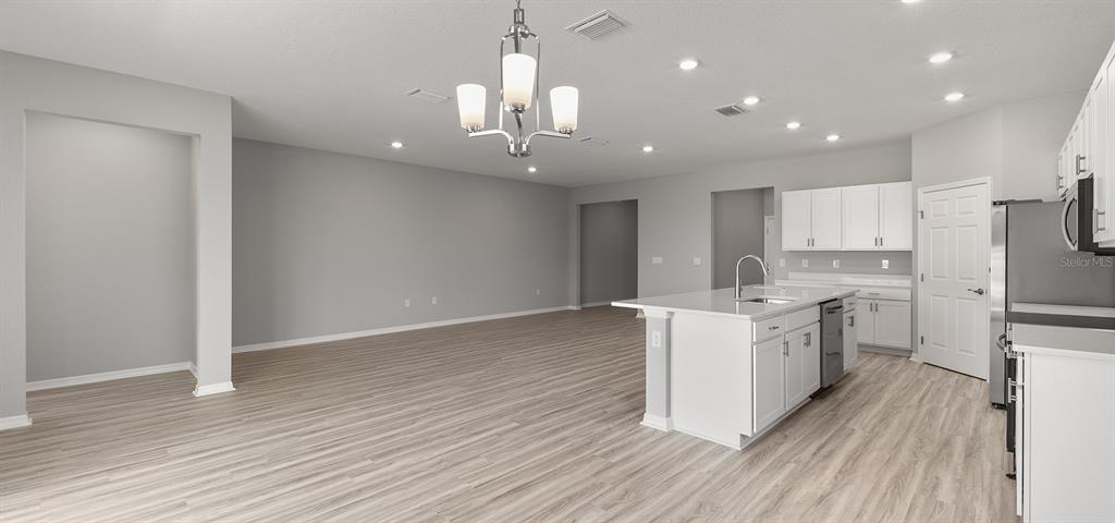 A kitchen with a white island and cabinets opens into a spacious, light-floored living area — 7658 SE 113TH PLACE, BELLEVIEW, FL
