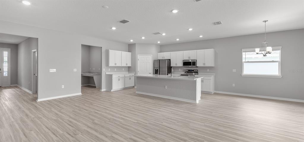 A bright, open-concept kitchen features white cabinetry, a central island, and light wood-look flooring — 7658 SE 113TH PLACE, BELLEVIEW, FL