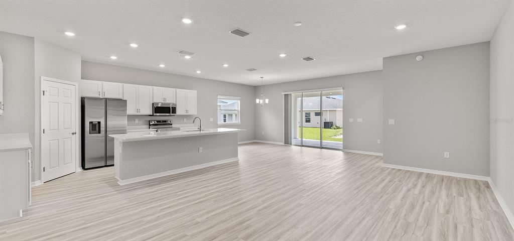 A modern open-concept kitchen and living area featuring white cabinetry, stainless appliances, and light flooring — 7658 SE 113TH PLACE, BELLEVIEW, FL