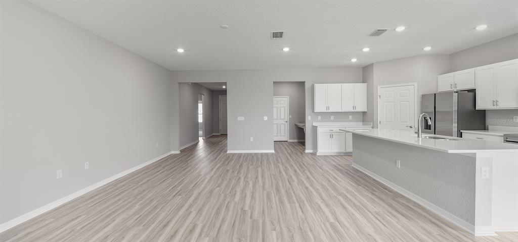 A bright, open-concept kitchen and living area features light wood-look flooring and white cabinetry — 7658 SE 113TH PLACE, BELLEVIEW, FL