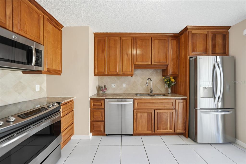 A kitchen features wood cabinets, stainless steel appliances, granite countertops, and white tile flooring — 20045 SANCRAFT AVENUE, PORT CHARLOTTE, FL