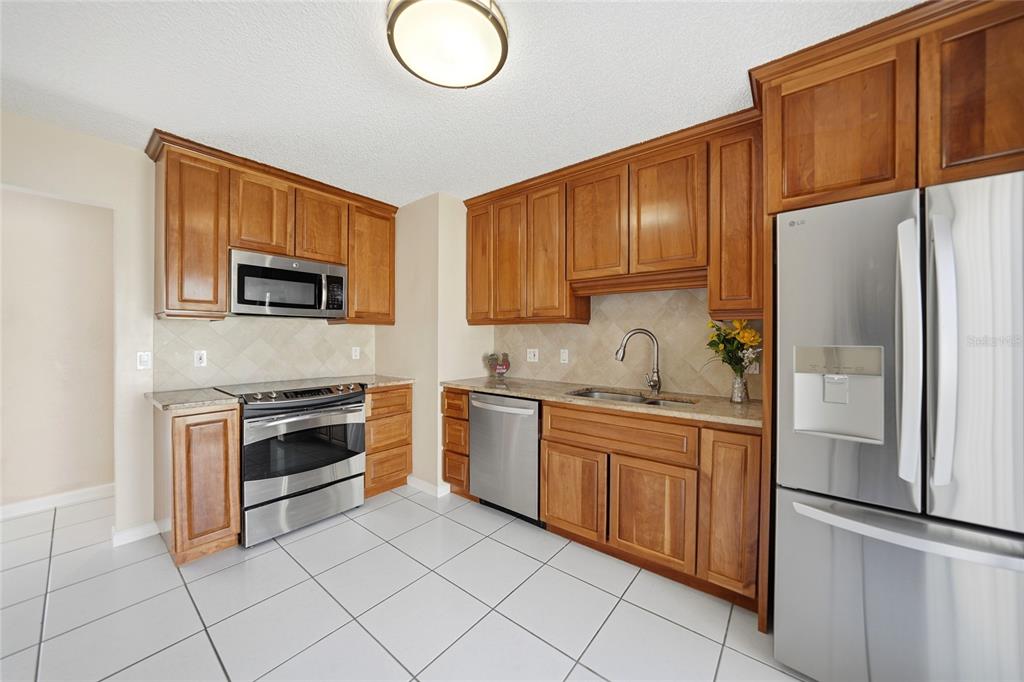 A kitchen with wooden cabinets, stainless steel appliances, tile flooring, and a tiled backsplash — 20045 SANCRAFT AVENUE, PORT CHARLOTTE, FL