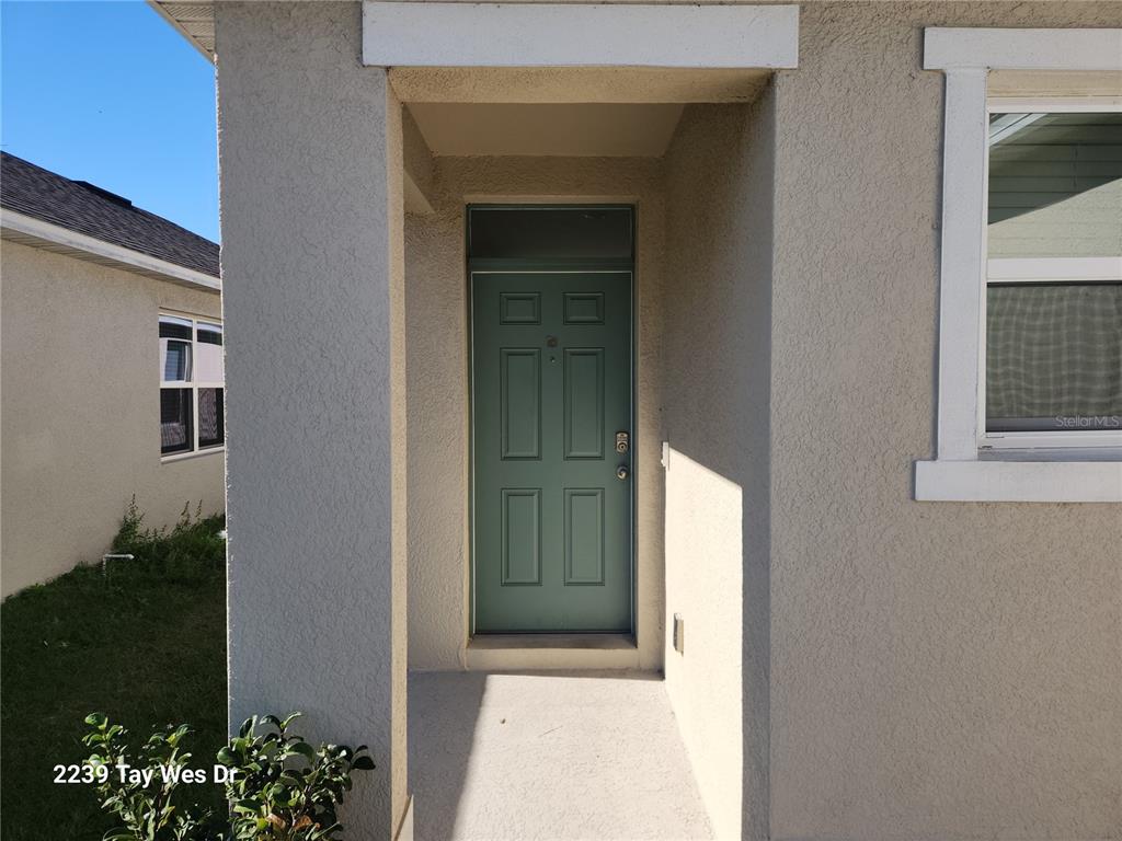 A teal front door is recessed within a covered entryway of a stucco house — 2239 TAY WES DRIVE, ST CLOUD, FL